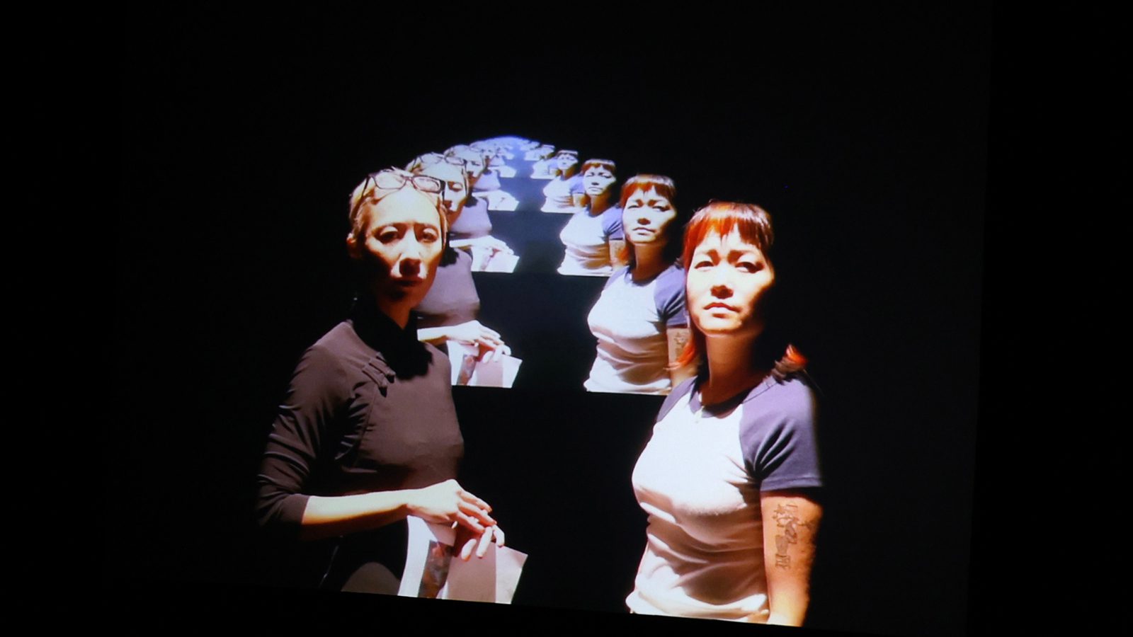 Two women face the camera and behind them is a the same image of the two women repeating into the horizon.