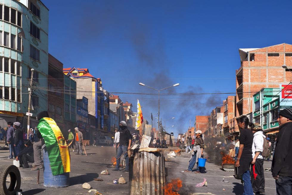 Protesters in Bolivia stand on the streets while some fires burn around them.