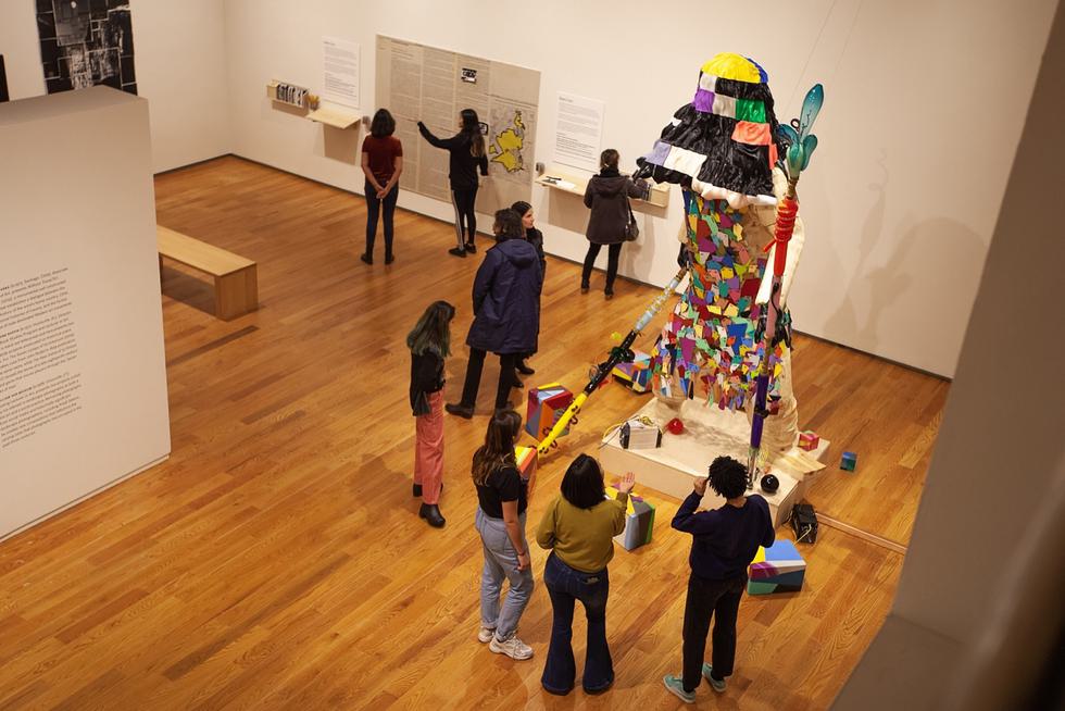 Nine students stand in a gallery in the Davis Art Museum. Five are looking at a colorful modern art statue while the rest are looking at artwork on the walls.