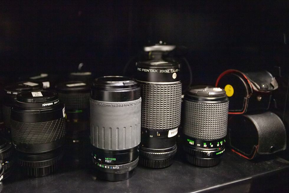 Five camera lenses sit on a black shelf.
