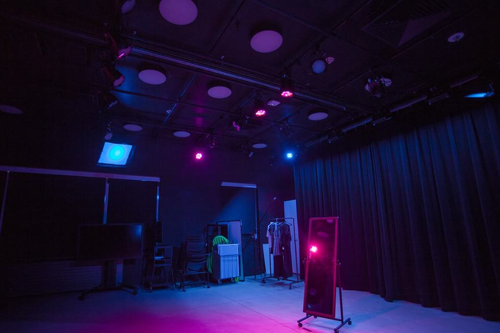A mirror sits in the middle of an empty stage. The whole picture is illuminated with pink and blue lighting.
