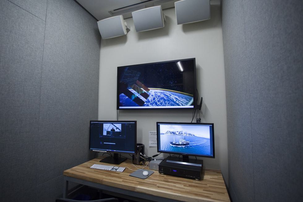 A private room with mounted speakers, a flat screen TV, and two monitors.