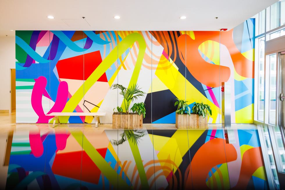 A wall with abstract mural art and its reflection on the floor.