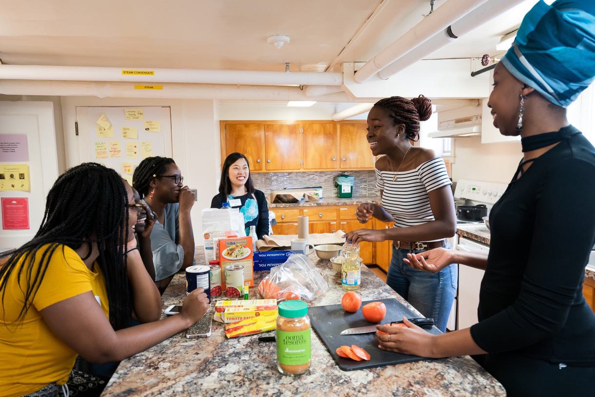 Students talk and laugh as they prepare food in a kitchen.