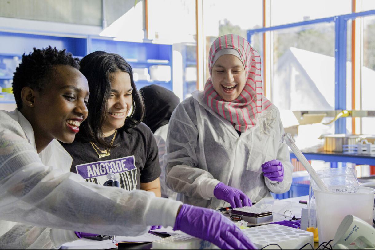 Three students laugh while working in a science lab.