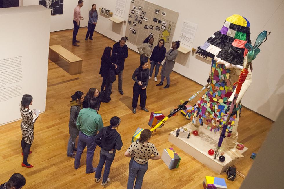 Looking down into an exhibition space with museum visitors and a tall, colorful, robot statue made of mahjong tiles.
