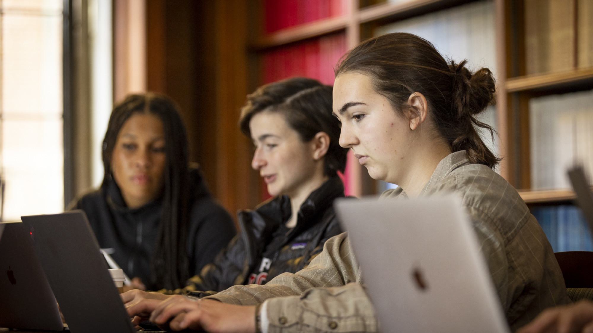 Three students work together on laptops around a table.