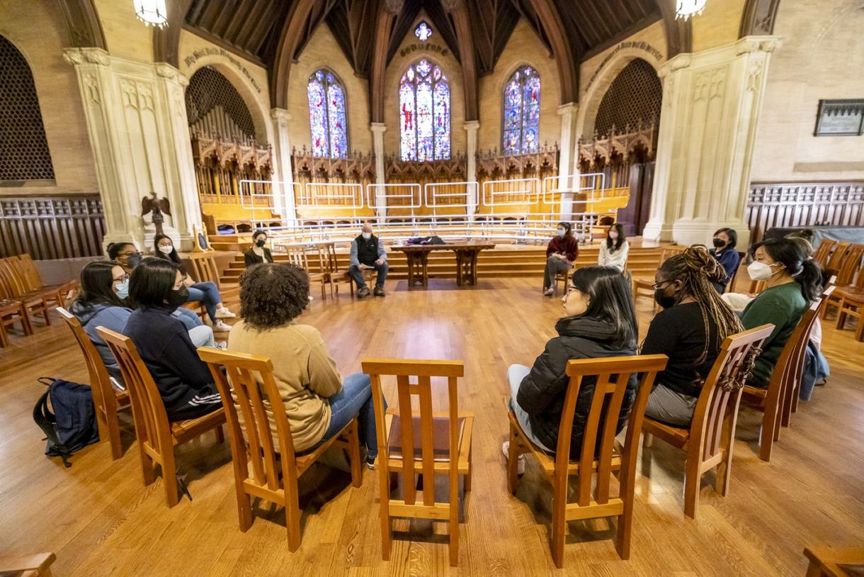 Students sit on wooden chairs in a circle inside a chapel.