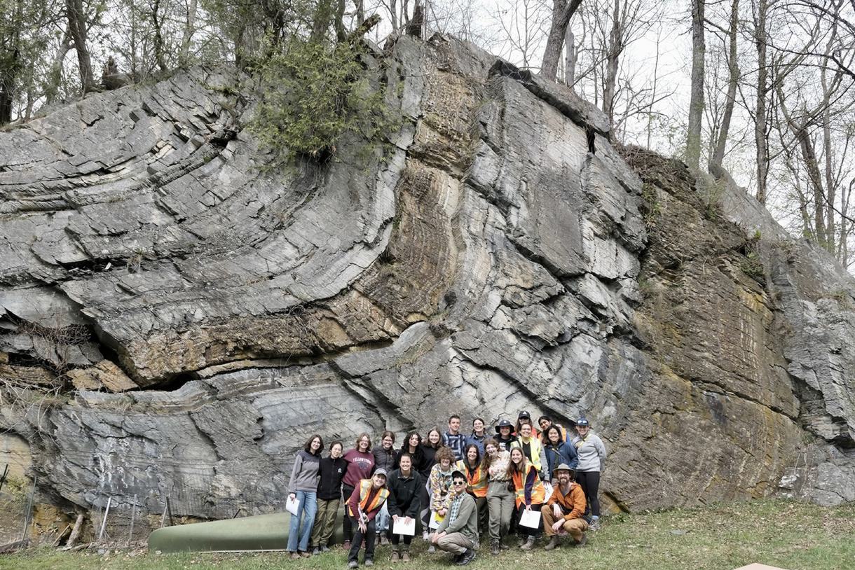 Group shot of a class standing in front of a large rock formation with a jagged ripple pattern.