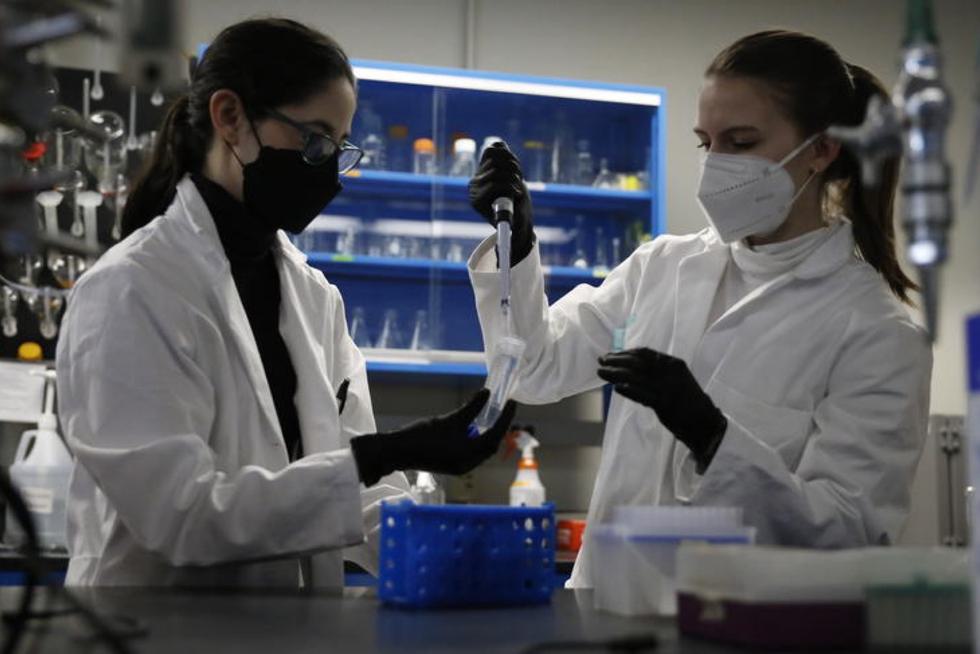 Two students in lab coats work to pipette into a tube.