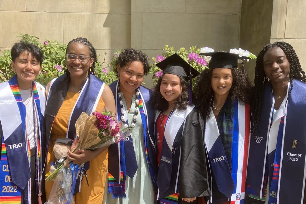 A diverse group of students pose in their graduation caps and gowns.
