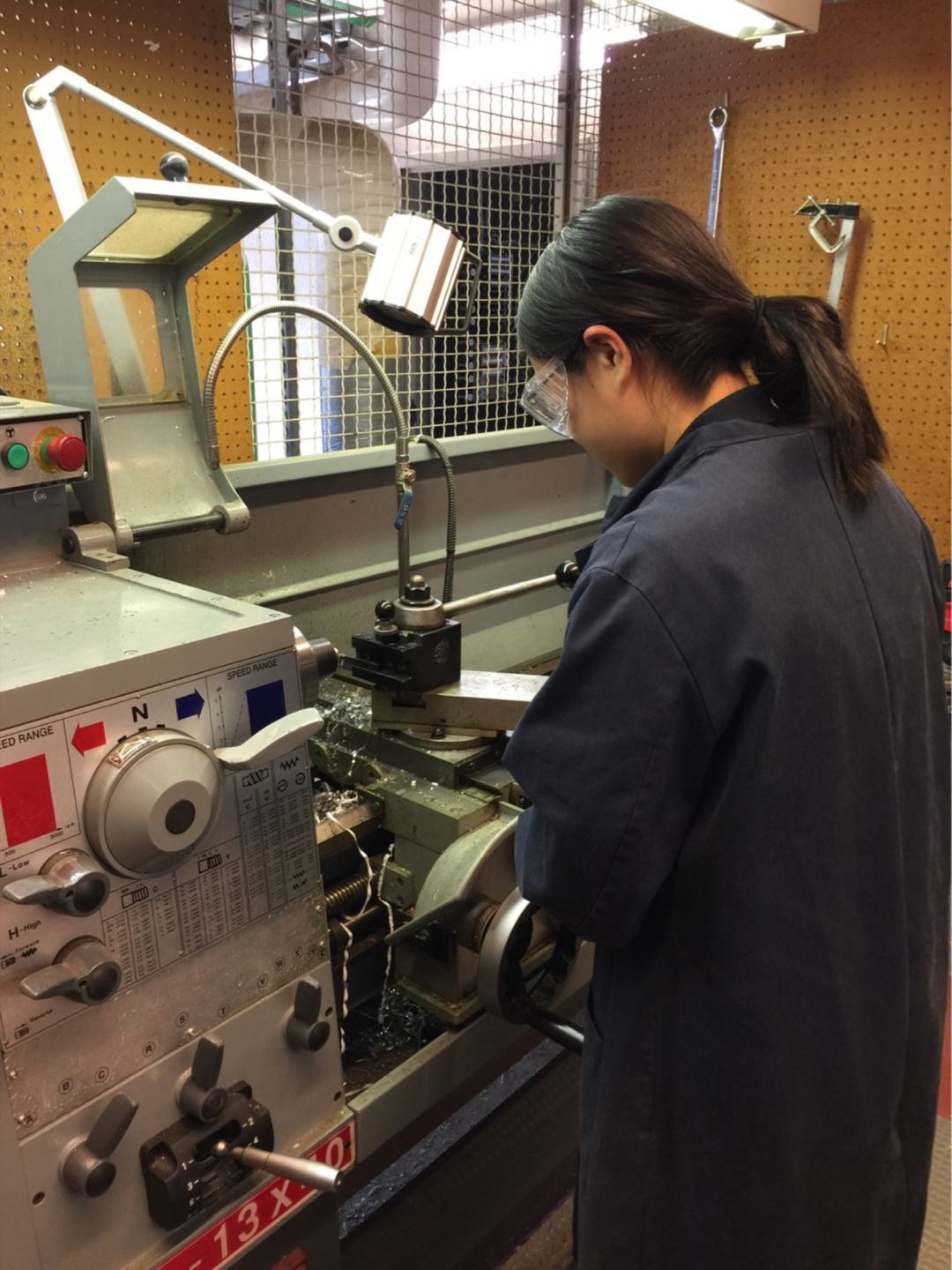 A student wearing protective glasses works on a lathe in the machine shop.