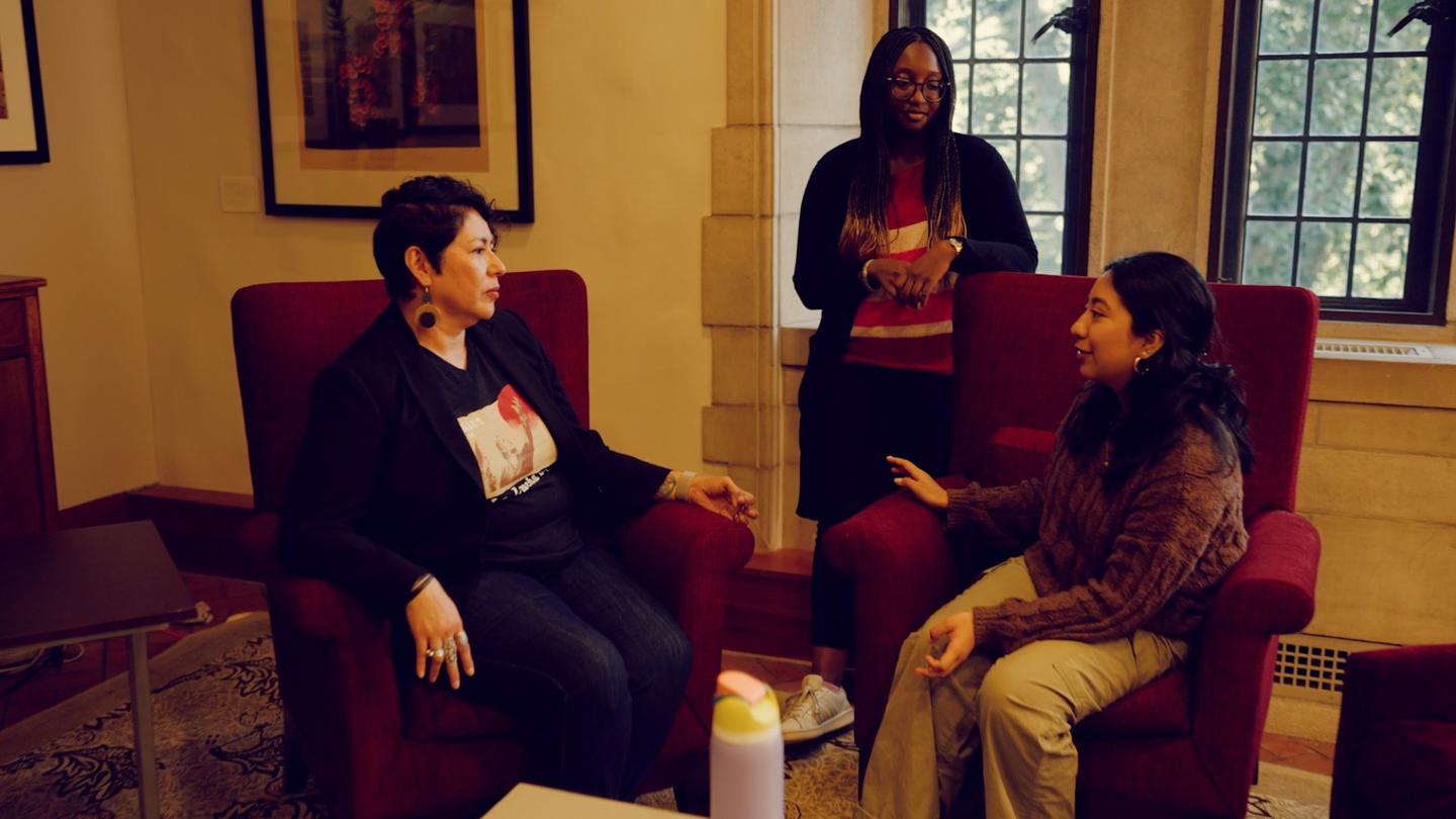 Two faculty members converse with a student in the Newhouse Center.