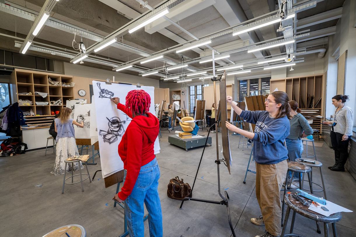 Students in an arts classroom use pastels to draw a reference in the middle of the room.