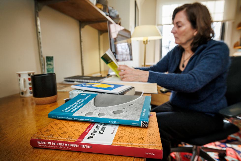 A faculty member reads at a table with books about ancient Greece and Rome.