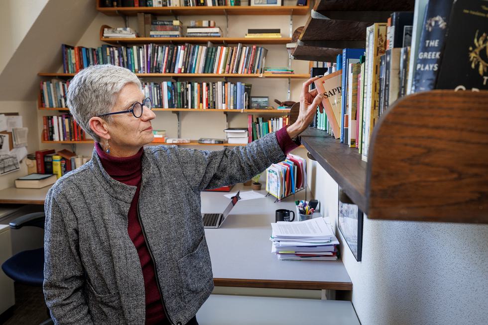 A faculty member pulls a book out from her bookshelf.