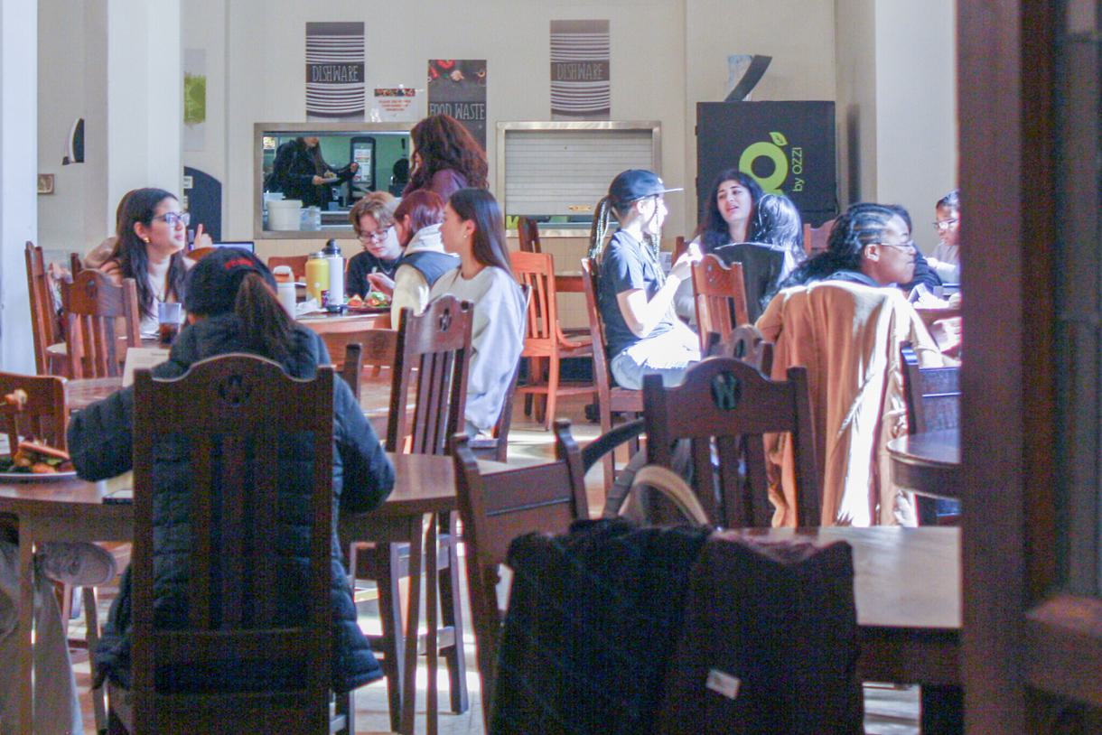 Groups of students eat around dark wood tables.