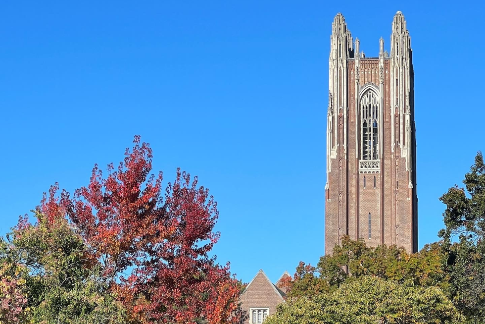 Wellesley bell tower peeking over fall-tinged leaves against a bright blue sky.