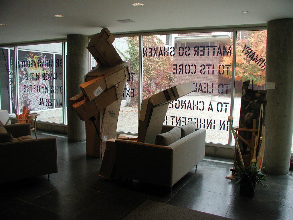 Installation view of tall cardboard sculpture in a gallery space with couches