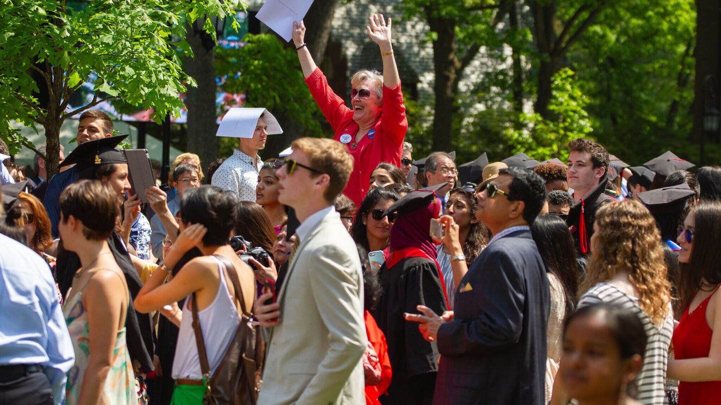 Parents and friends of graduates cheer for graduates outside on a sunny day.