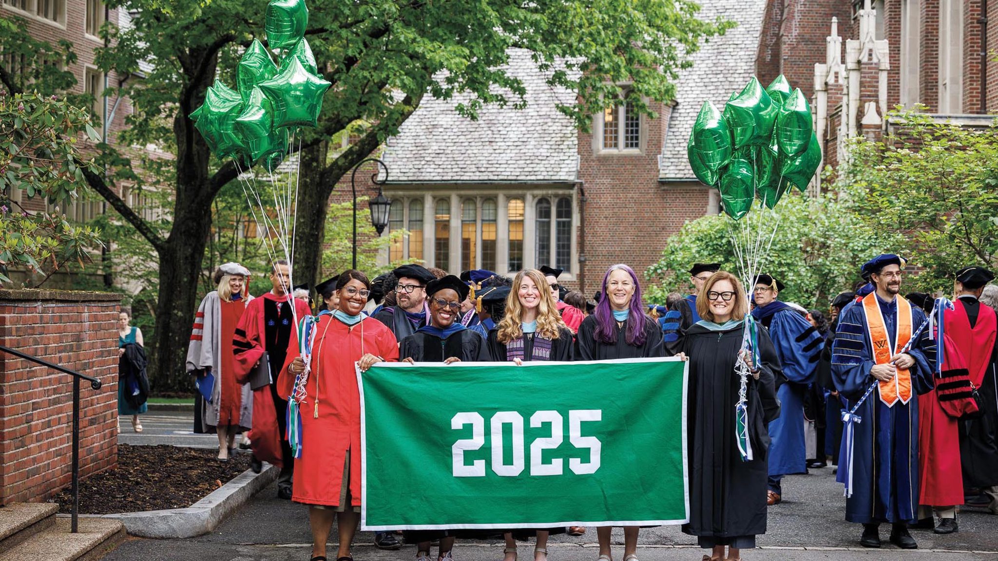 A photo of faculty holding the green class banner of 2025 before the procession