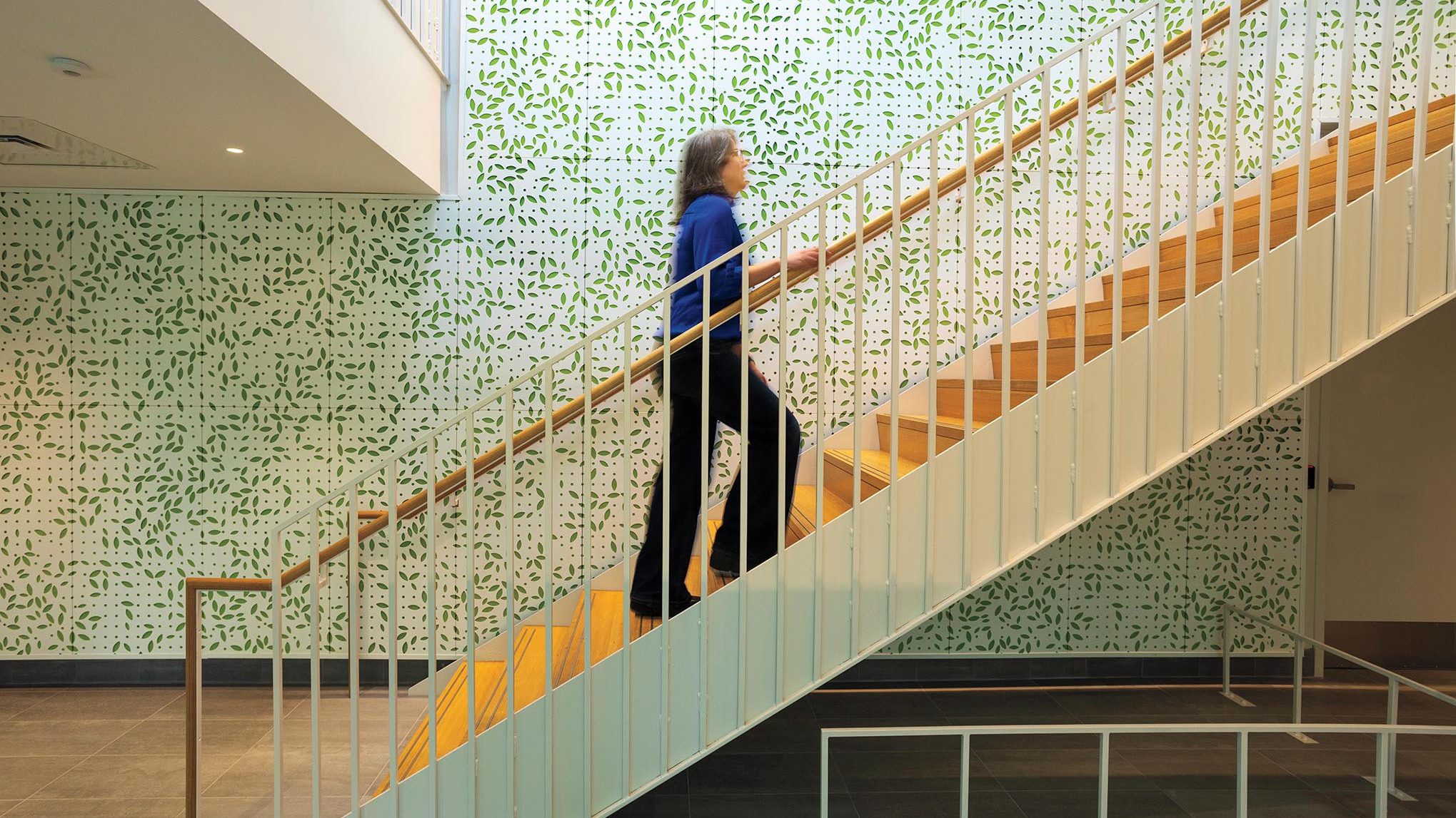 A person goes up a modern staircase with a green modern wall treatment that evokes leaves