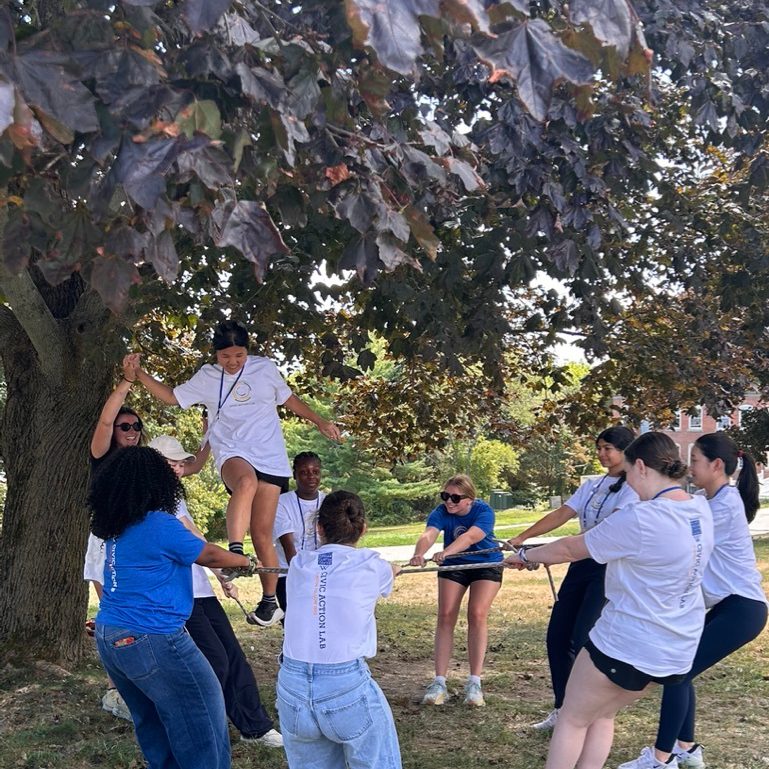A student balances on a rope that her teammates are pulling taught.
