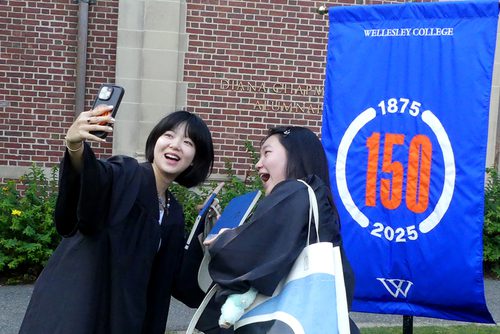 Two students pose for a selfie in front of the college’s 150 banner.