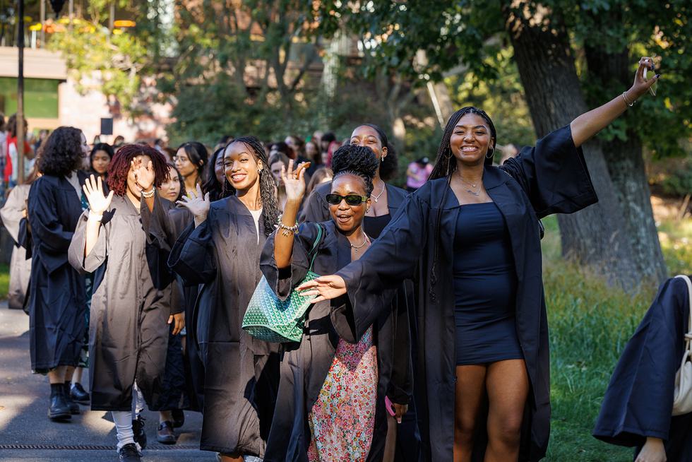 Students wearing graduation gowns pose for the camera with their arms up and in the air