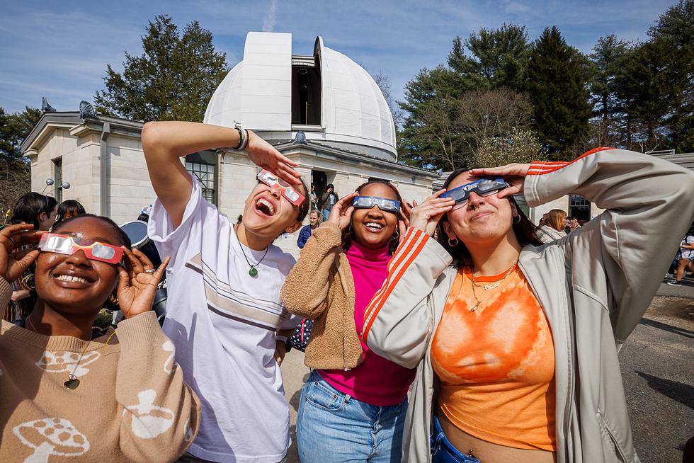 Four students wearing protective glasses look up at the eclipse.