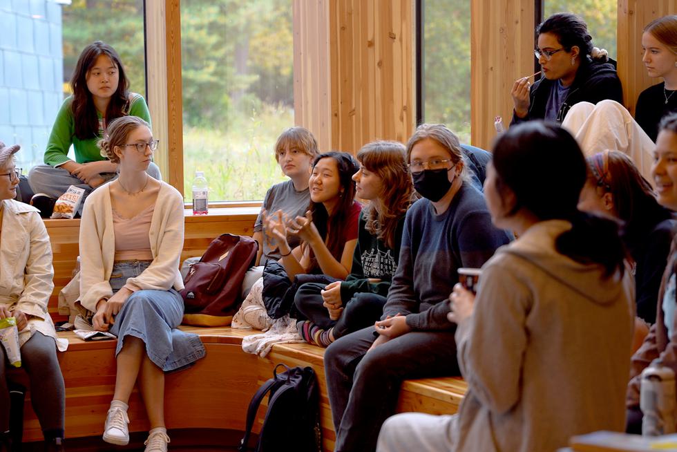 A group of students sit on steps inside the science center and talk during a Green Gathering