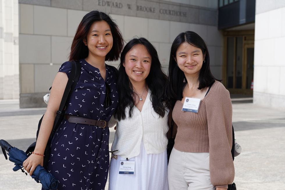Three interns pose for a photo in front of the Edward Brooke Courthouse in Boston.