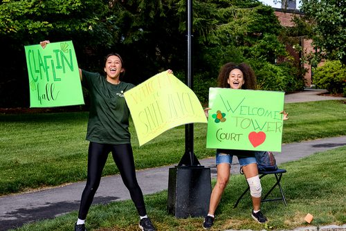 Two students cheer and hold welcome signs for families moving onto campus.