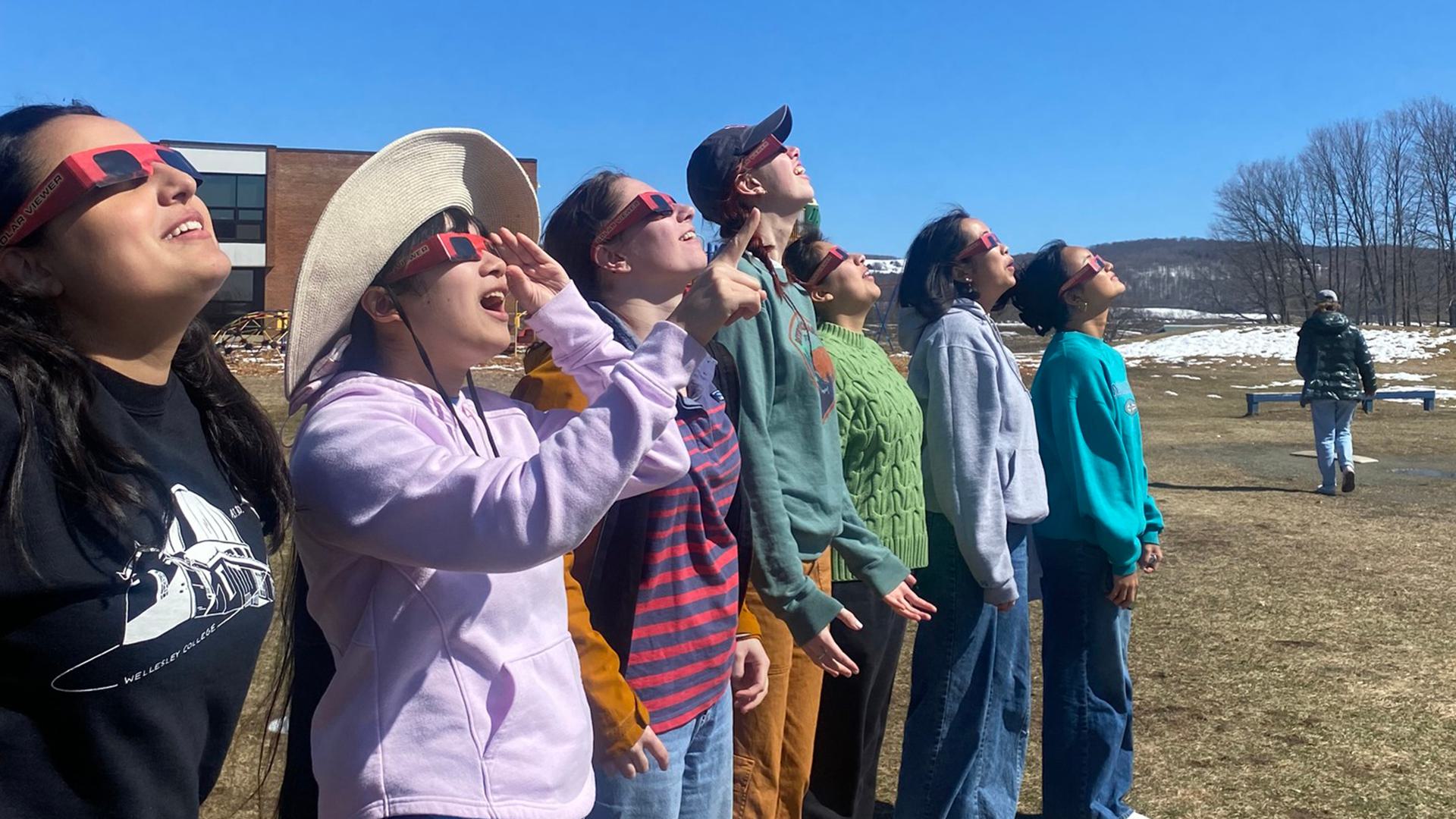 Students wearing protective glasses gaze up at the eclips.