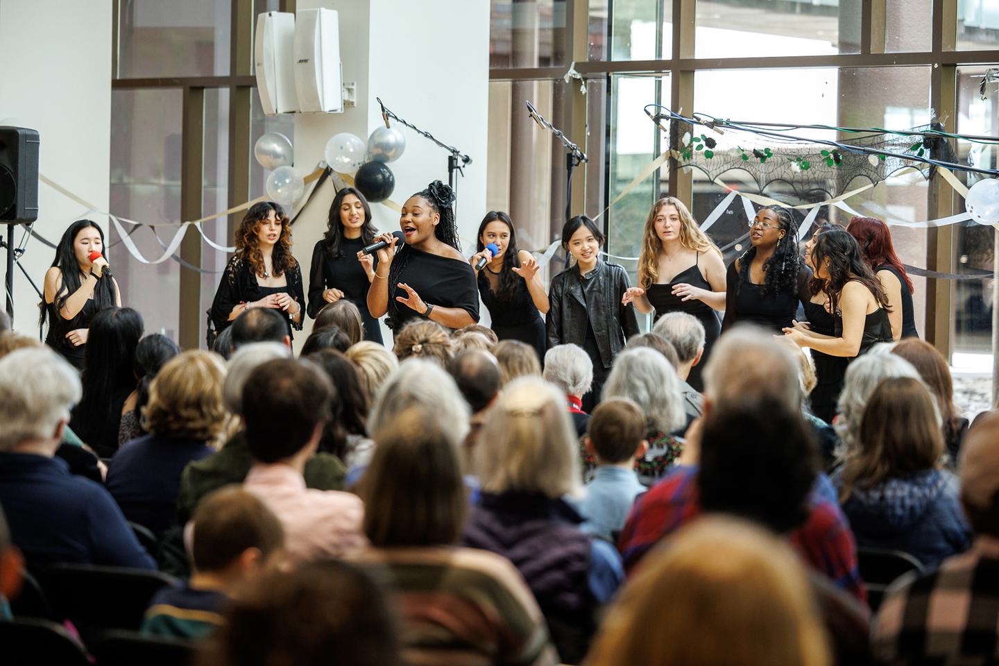 A group of students stand in front of an audience and sings.