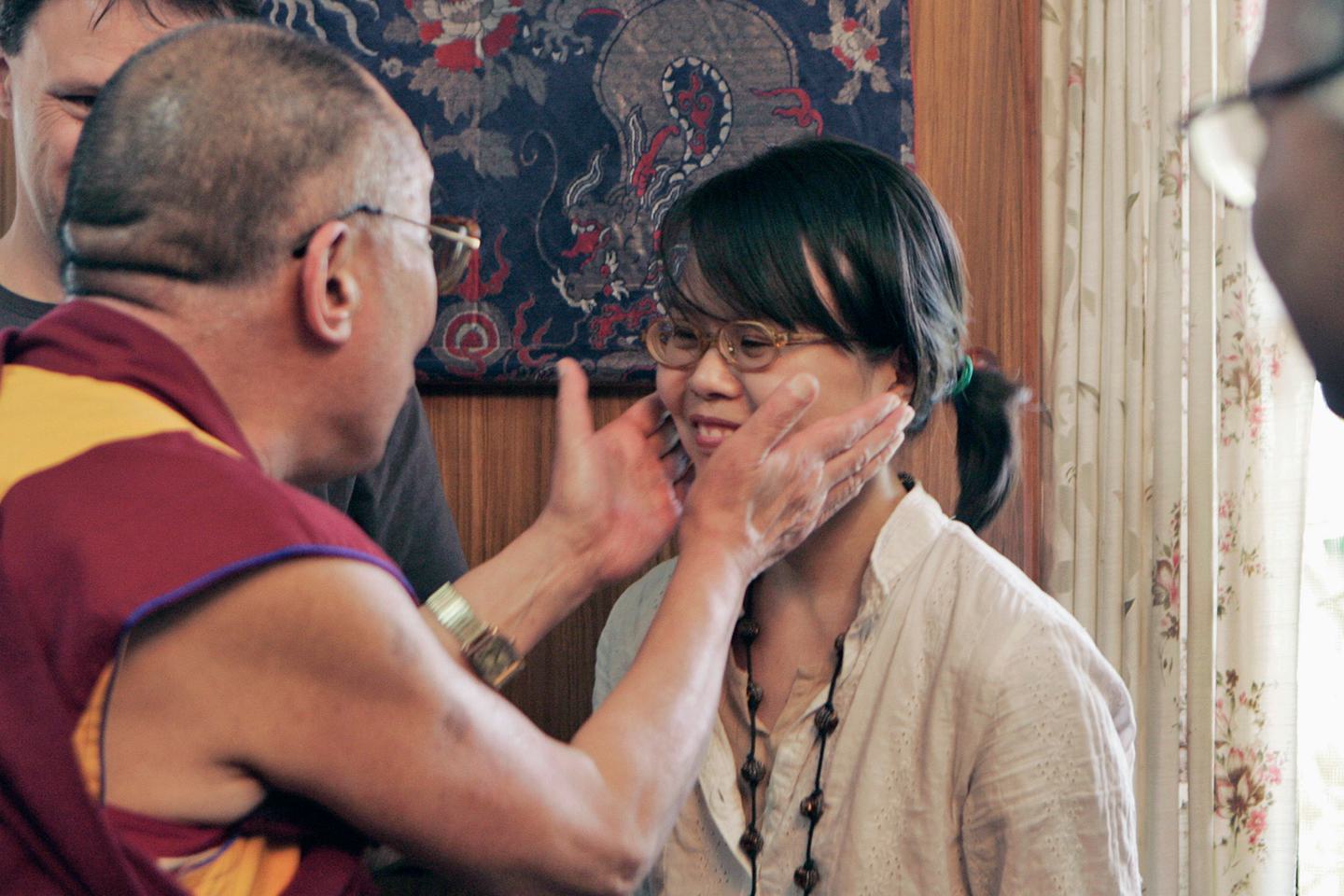 The Dalai Lama holds Amy Yee’s face in his hands as Yee laughs