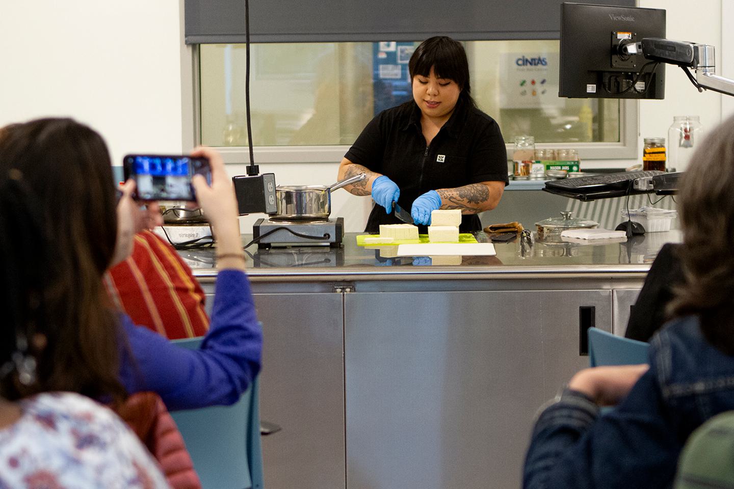Bettina Makalintal ’14 cuts tofu in front of an audience in the cooking lab.
