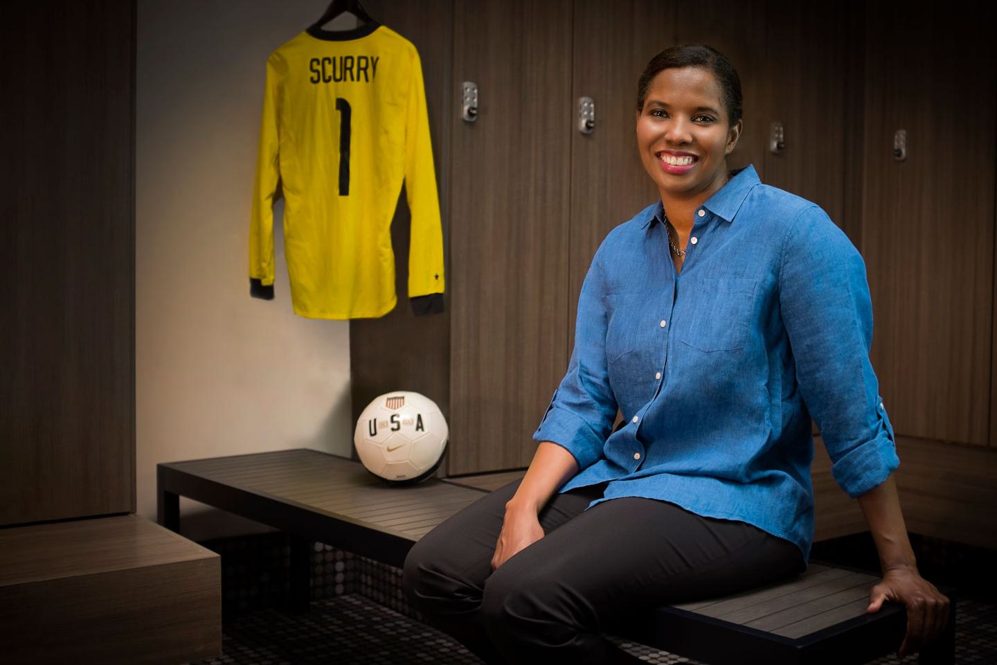 Briana Scurry posing on a bench with a soccer ball and jersey next to her