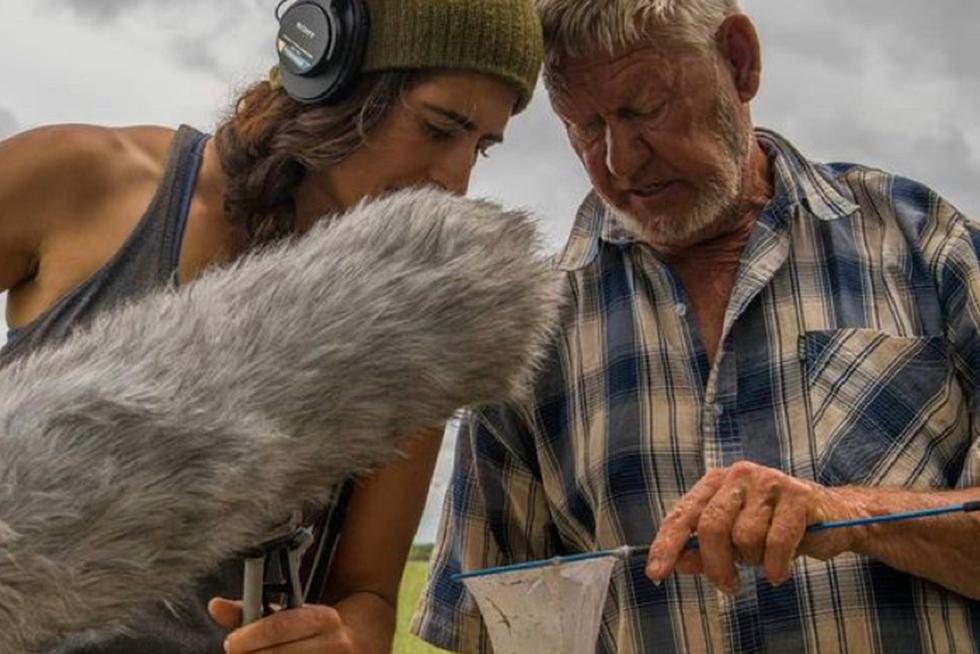 Cat Jaffee holds a microphone and leans toward a man holding a fishing net.