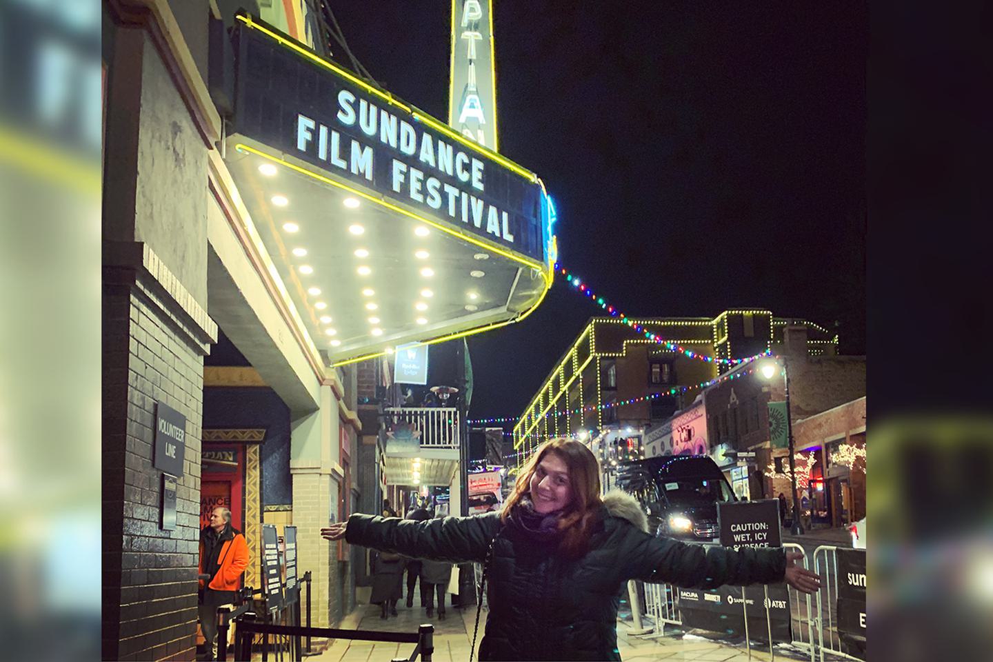Claire Ayoub stands outside a Sundance sign with her arms outstretched.