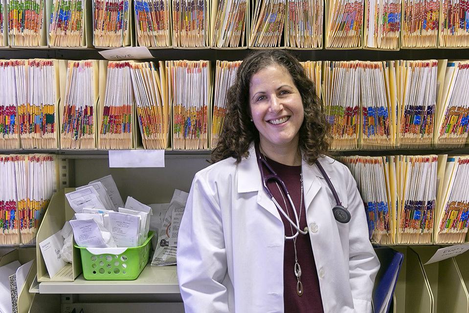 A woman in a white lab coat stands in front of rows of files.
