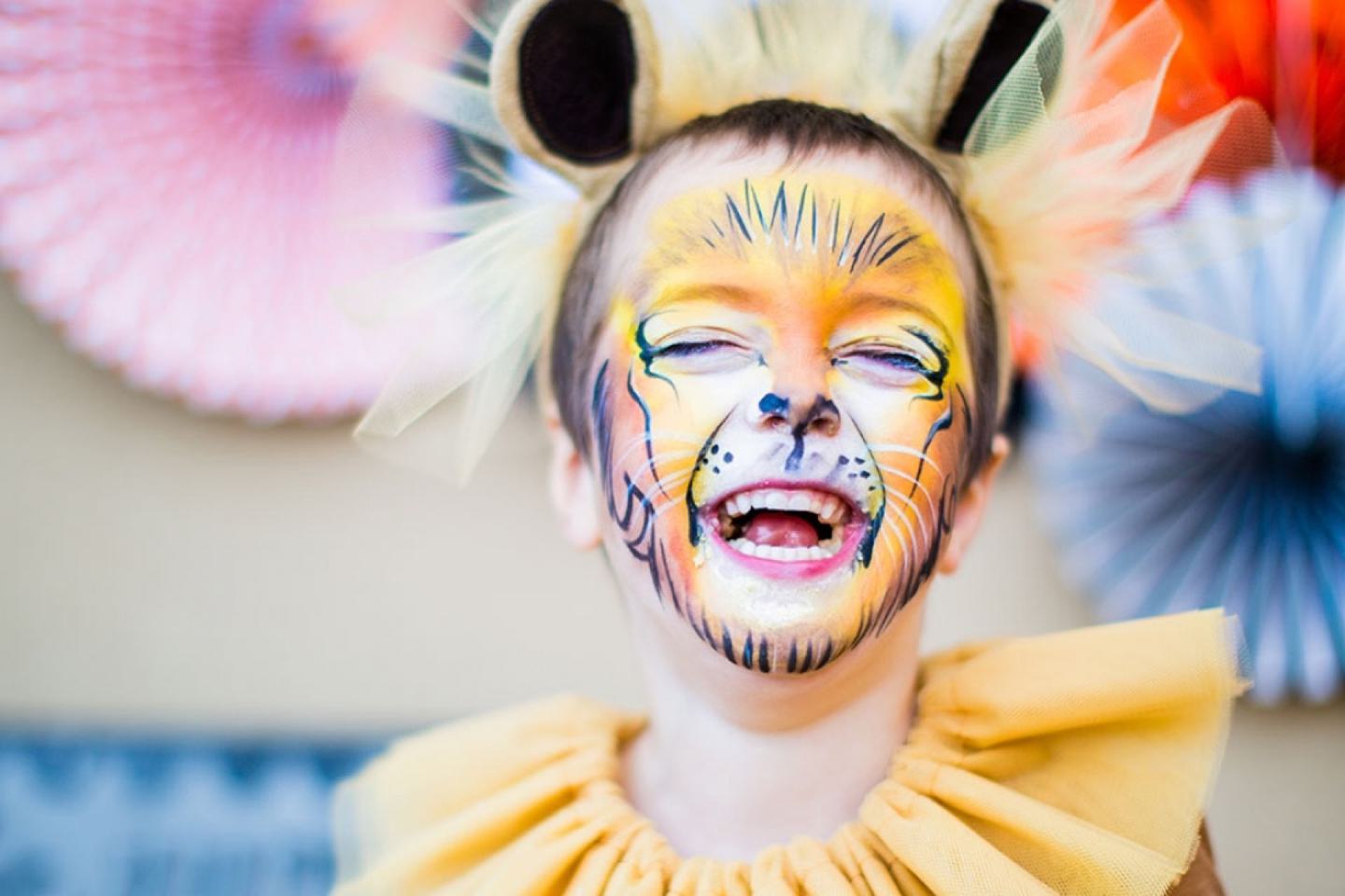 Child dressed in a lion costume and lion face paint laughs
