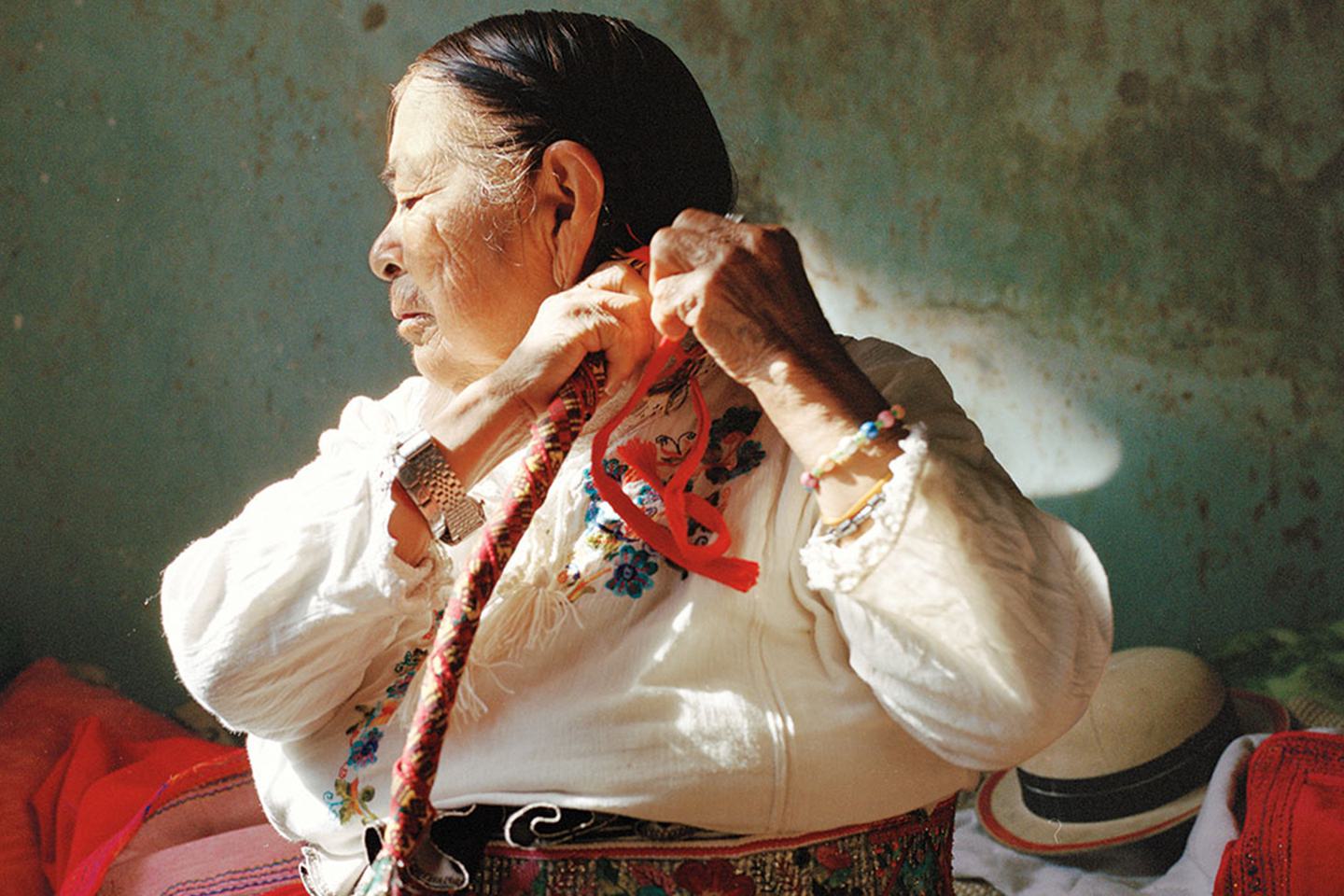 A photo of an older Hispanic woman braiding her long hair.