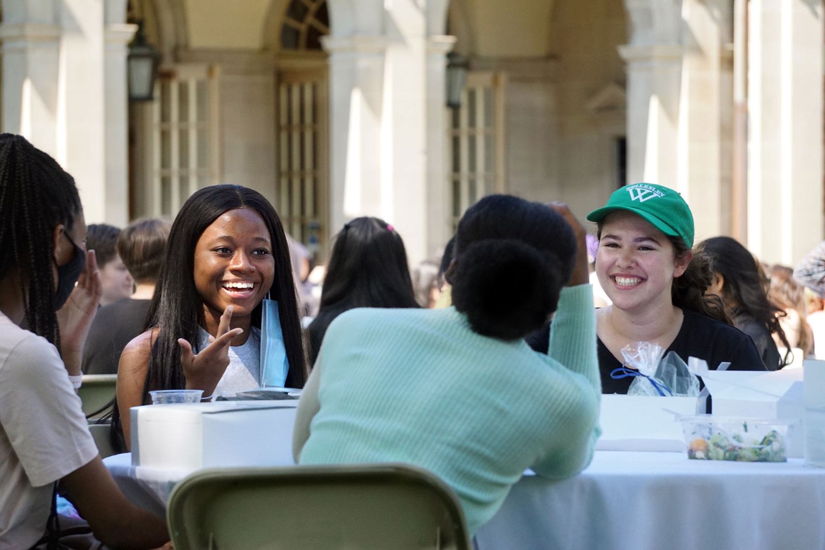 students smiling and eating together at an outdoor table