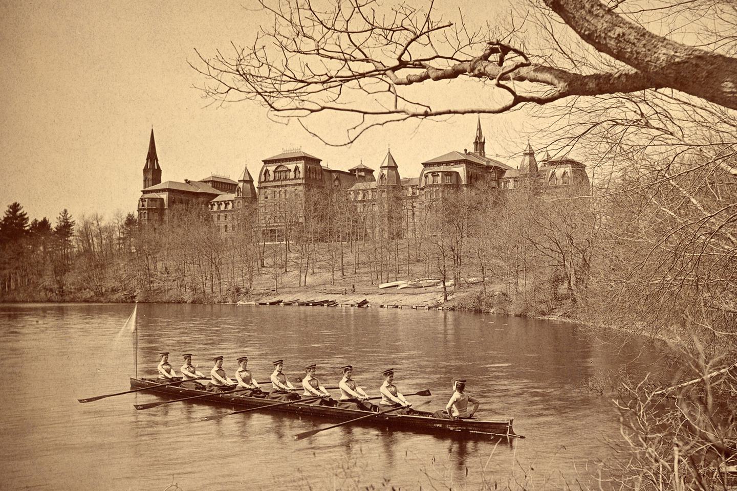 The class crew of 1894 rows on Lake Waban, with College Hall in the background.