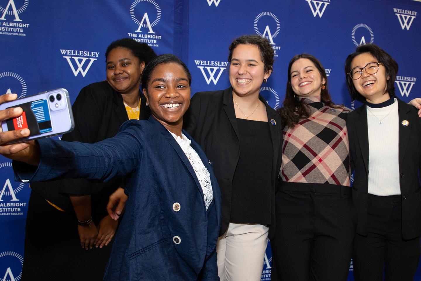 Five students pose for a selfie in front of the Albright Institute drop cloth background.
