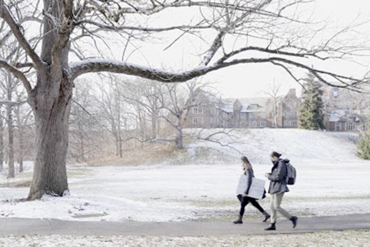 Two students walk across a snowy campus.