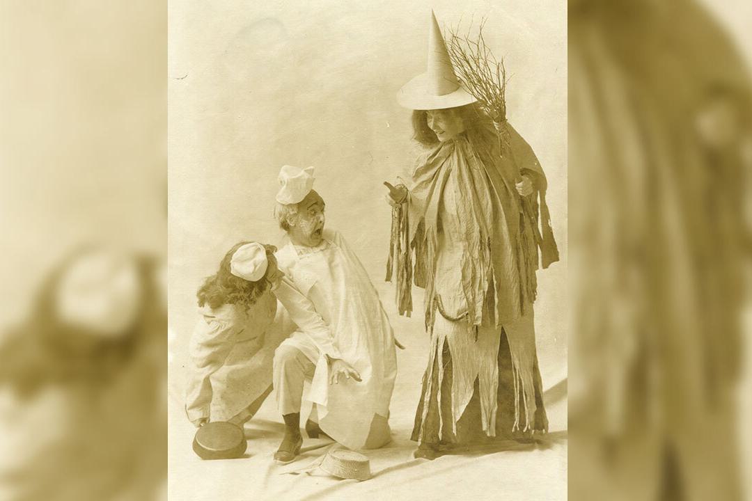 A theater photo from 1906 showing three students re-enacting a scene. The student at right is dressed as a witch.