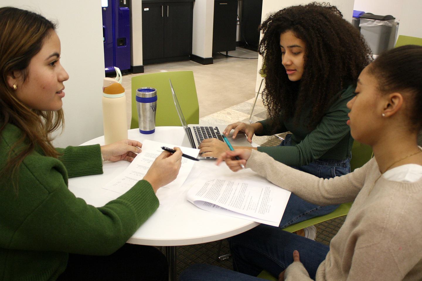 Three students sit at a table looking over papers.