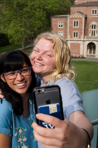 Two Wellesley College students take a selfie in front of Diana Champman Walsh Alumnae Hall